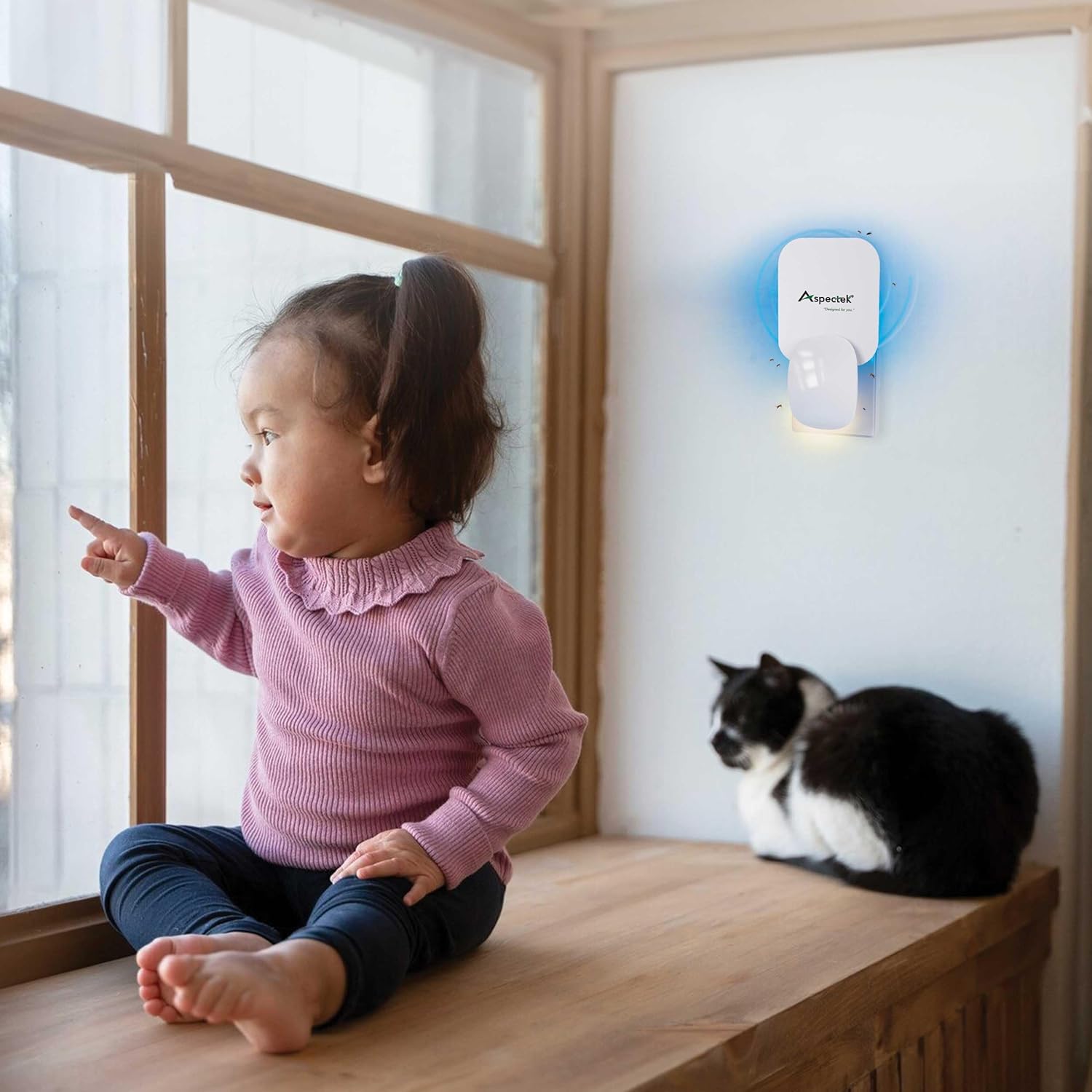 Child pointing at a wall-mounted device with a cat sitting nearby.
